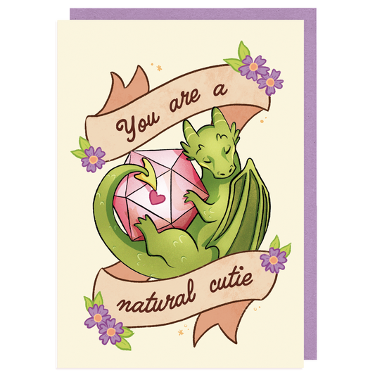 A product mockup of a D&D themed postcard. It pictures a dragon with a D20 dice and text saying ''you are a natural cutie''
