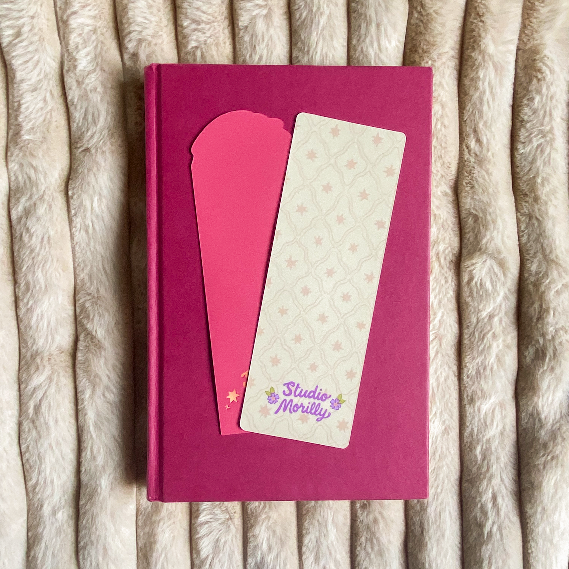 A product mockup of a bookmark with an illustration of a green dragon holding a D20 dice. There is text saying ''you are a natural cutie''. The bookmark is laying on a book